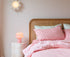 Bedroom with pink bedding and a nightstand with a lamp.
