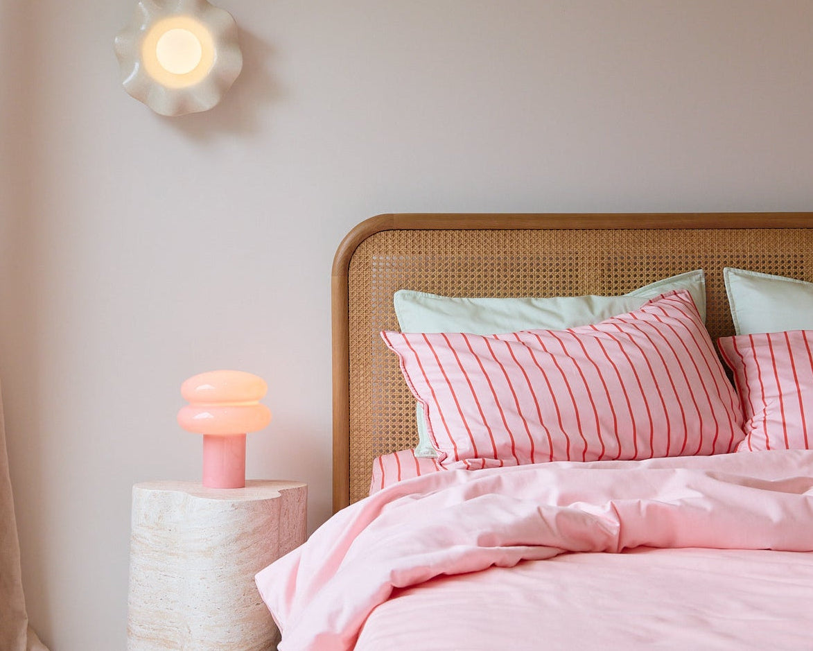 Bedroom with pink bedding and a nightstand with a lamp.